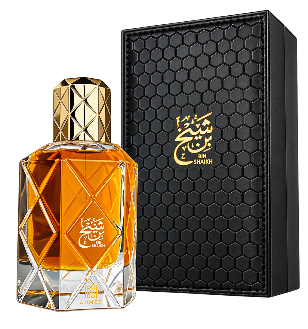 A faceted glass perfume bottle filled with amber-orange liquid, shown beside a black rectangular presentation box with a gold honeycomb texture and gold Arabic script reading BIN SHAKKH.