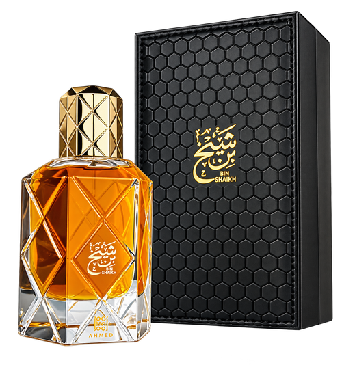 A faceted glass perfume bottle filled with amber-orange liquid, shown beside a black rectangular presentation box with a gold honeycomb texture and gold Arabic script reading BIN SHAKKH.